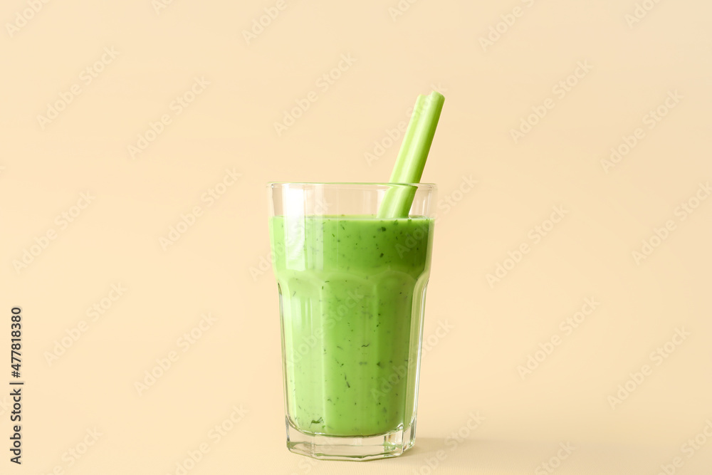 Glass of green juice with celery on beige background