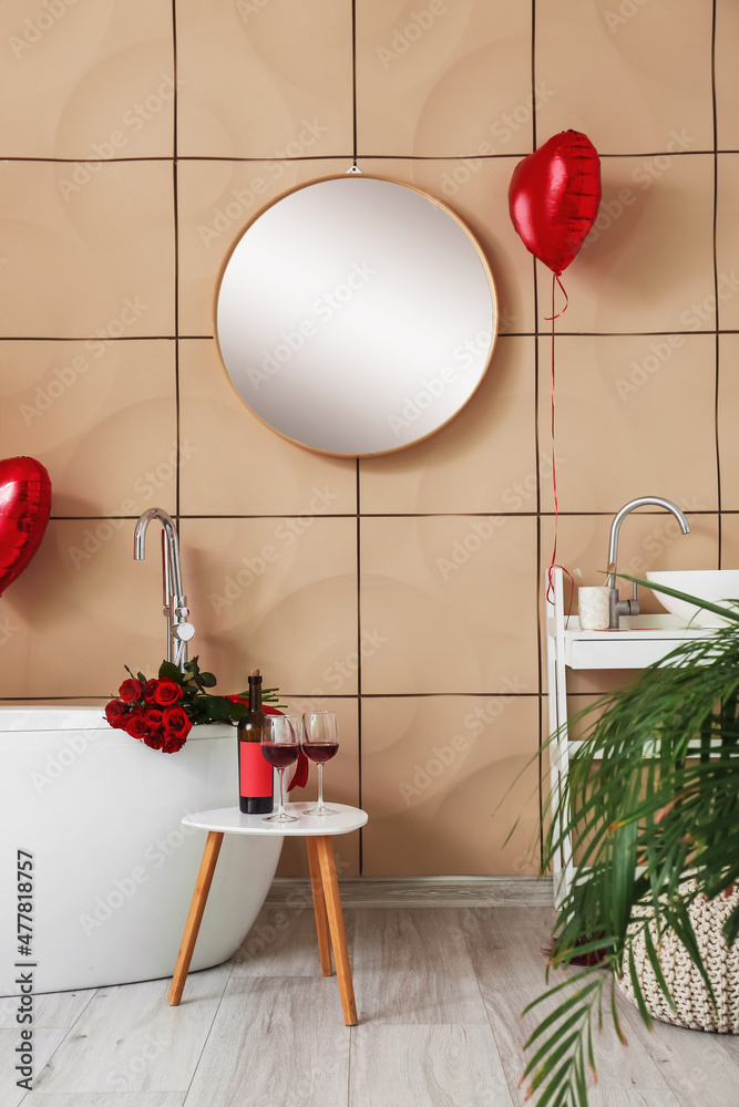 Bottle of wine and glasses on table in bathroom decorated for Valentines Day