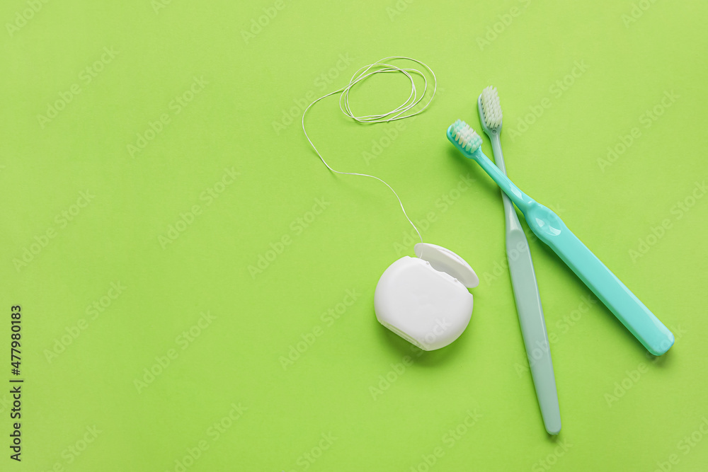 Dental floss and toothbrushes on green background