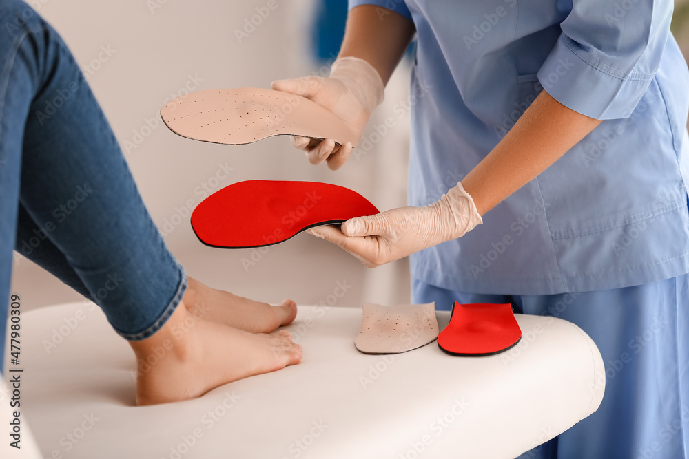 Female orthopedist showing insoles to patient in clinic