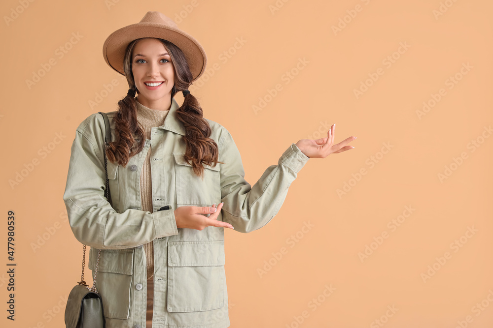 Young fashionable woman pointing at something on color background