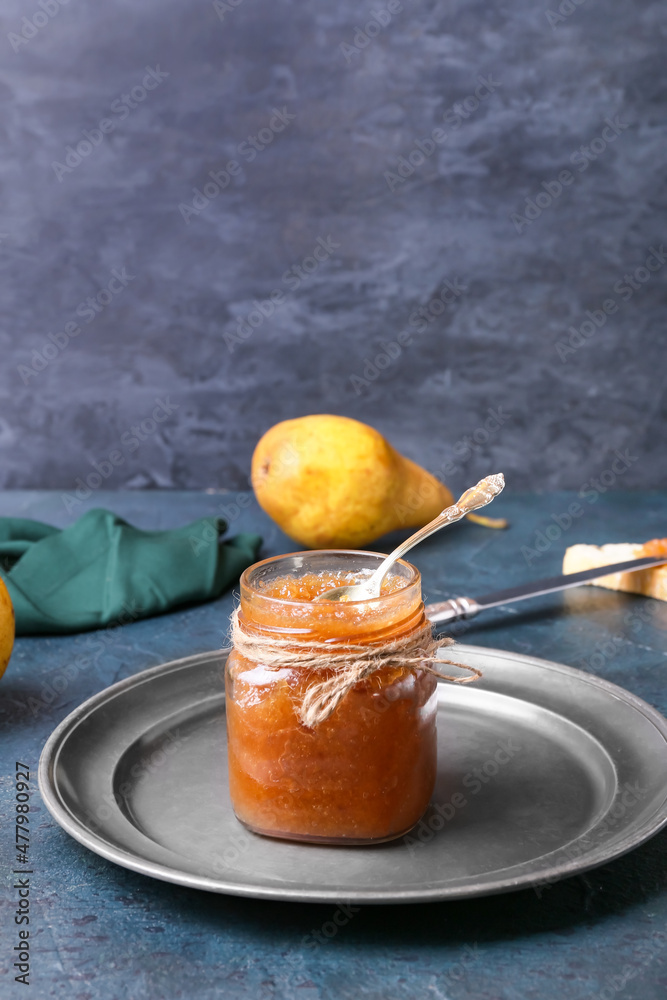 Plate with glass jar of tasty pear jam on dark background