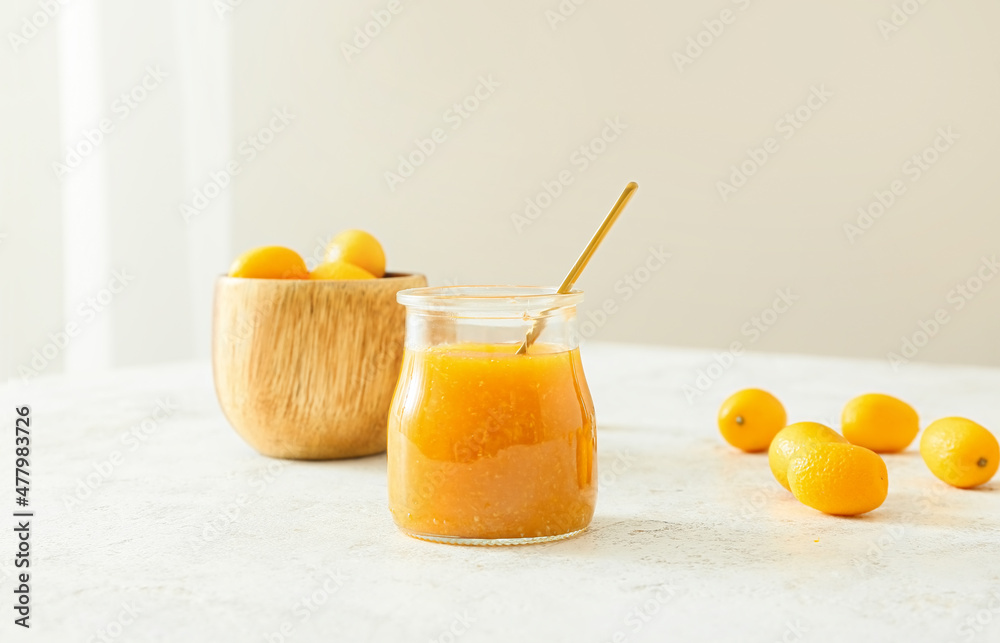 Jar of tasty kumquat jam and fresh fruits on light background