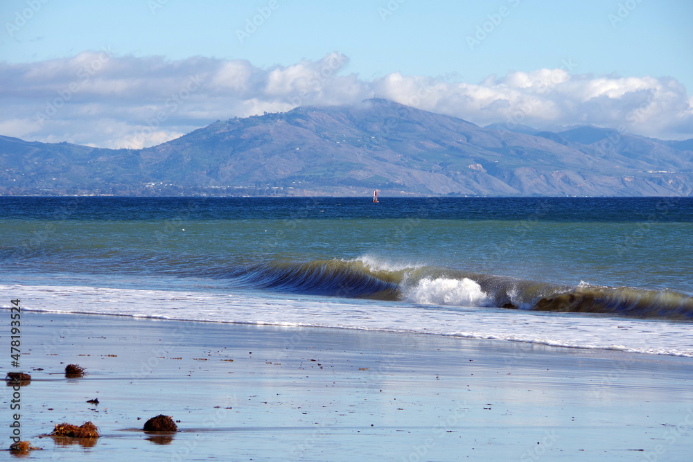 Panoramic winter ocean beach scene in Santa Barbara, California, with mountains and clouds in the ba