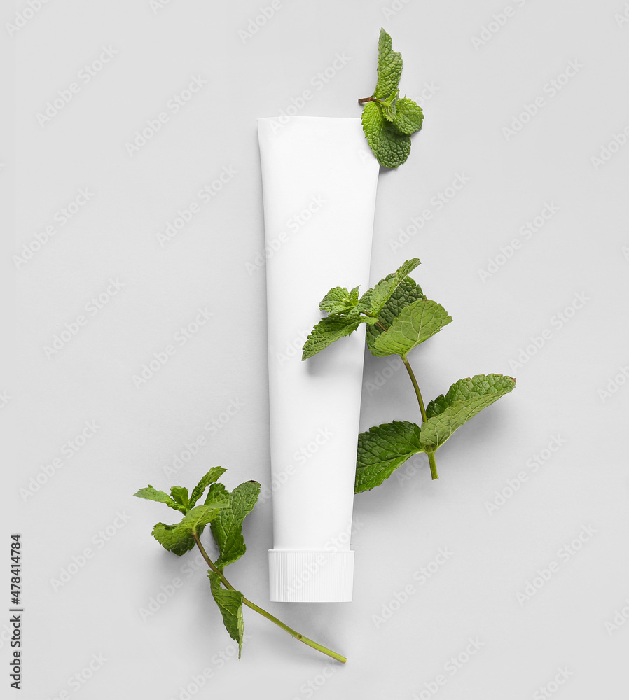 Tube with tooth paste and mint on light background