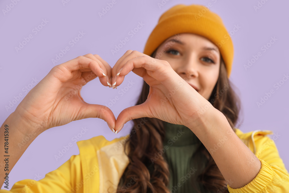 Woman in raincoat showing heart gesture on color background