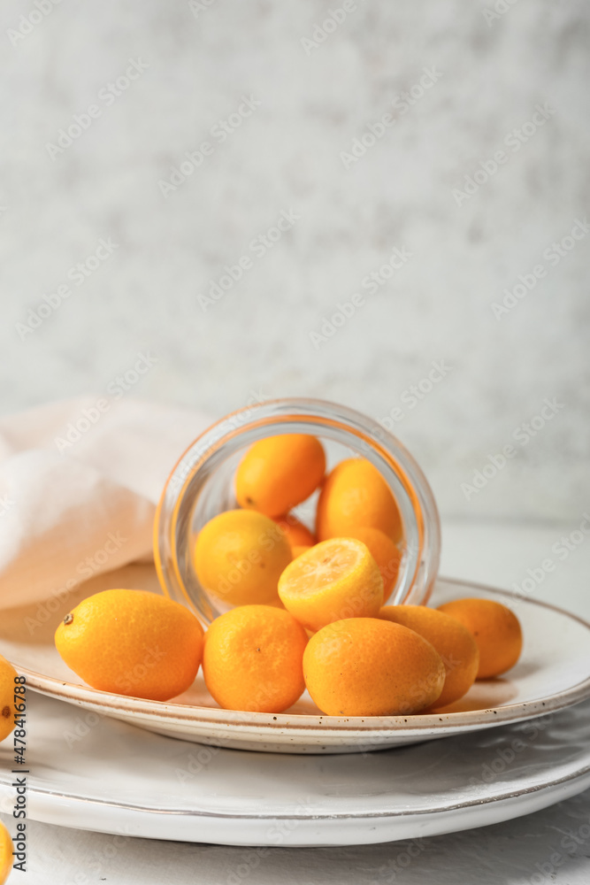 Jar with tasty kumquat fruits on light background