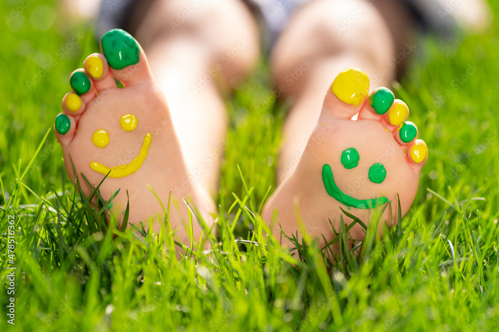 Happy child with smile on feet lying on green spring grass