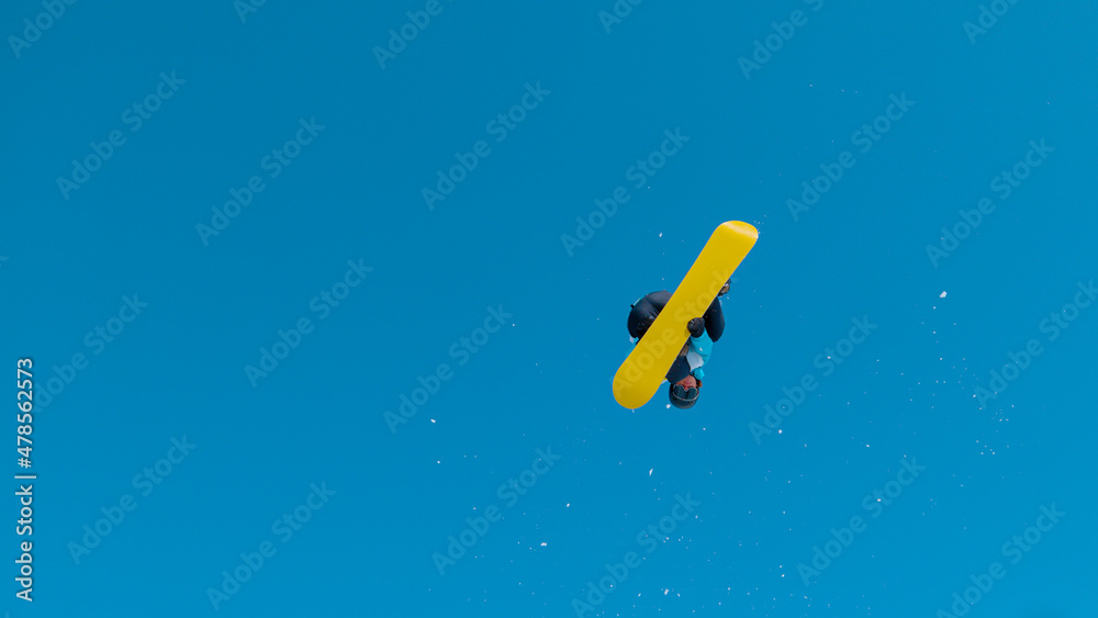 BOTTOM UP: Athletic snowboarder flying through the air and doing a 360 grab.