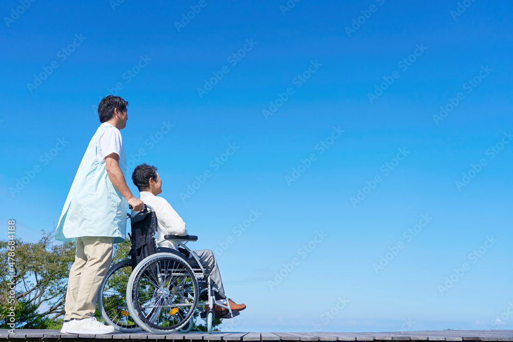 介護士と車椅子に乗る高齢者　屋外