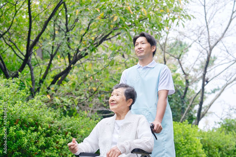 介護士と車椅子に乗る高齢者　屋外