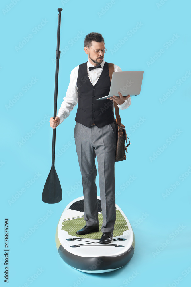 Businessman with laptop standing on sup board against color background