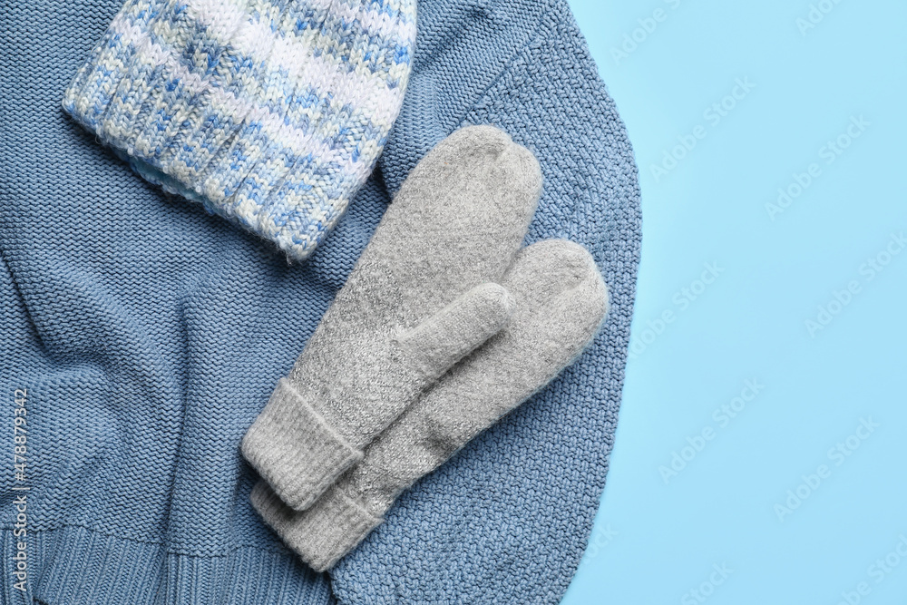 Warm mittens, sweater and hat on color background, closeup