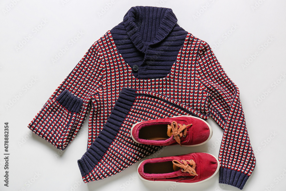 Stylish childrens sweater and shoes on light background