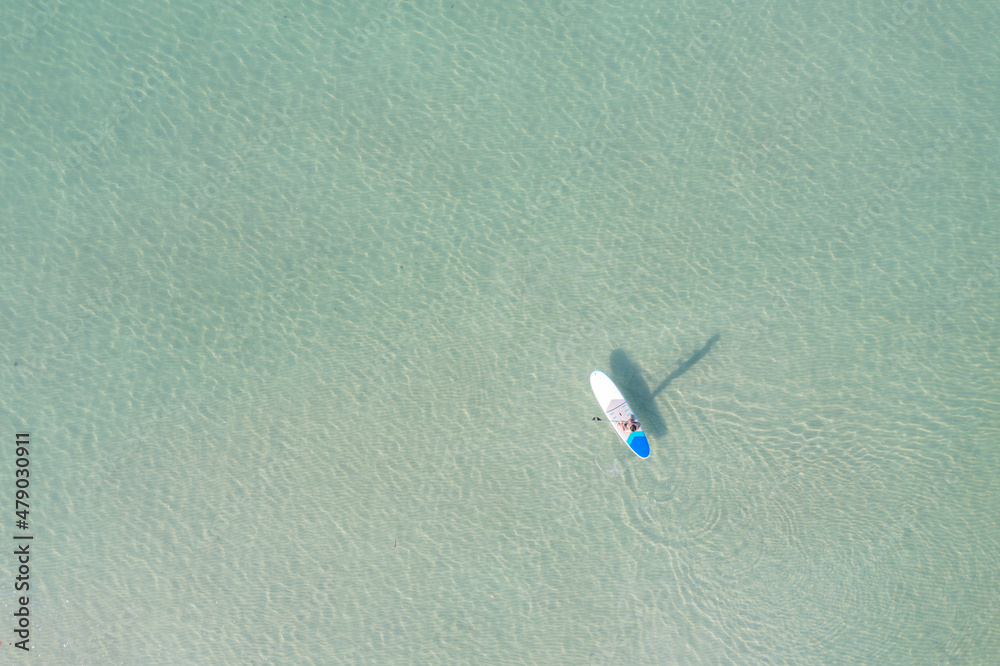 夏日，一名亚洲男子在碧绿的热带清澈水域锻炼冲浪板的鸟瞰图。