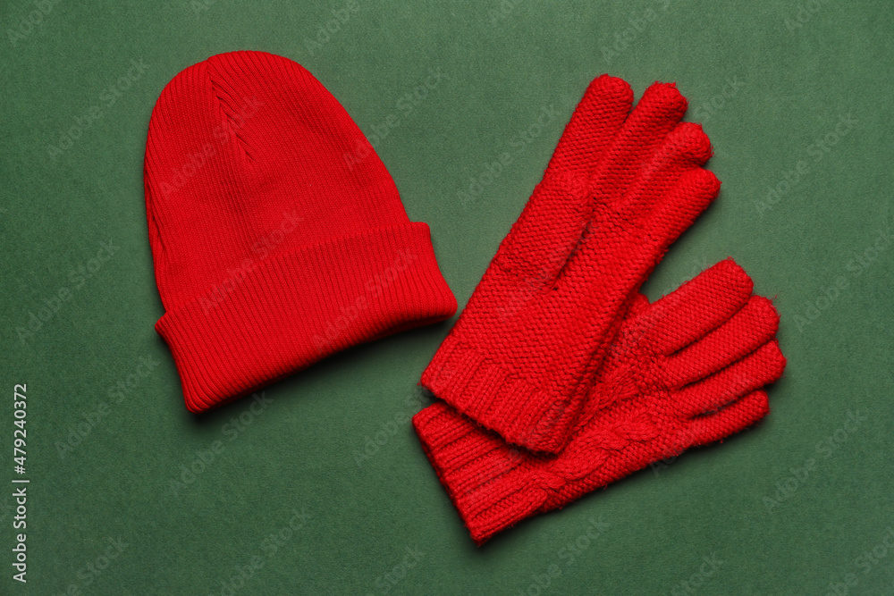 Red knitted gloves and hat on green background