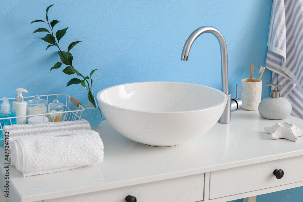 Table with sink, plant branch in vase and bath supplies near blue wall