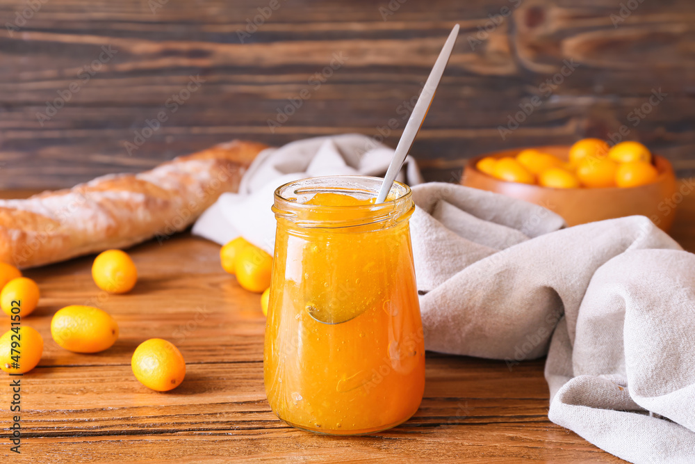 Jar of tasty kumquat jam and fresh fruits on wooden background