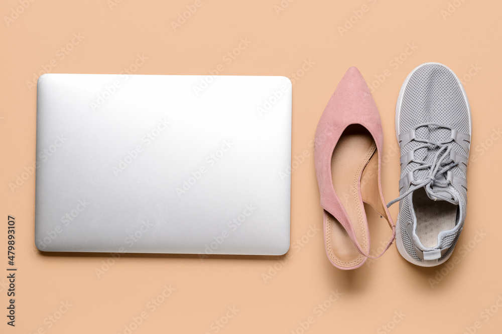 Laptop with high-heeled and sports shoes on color background