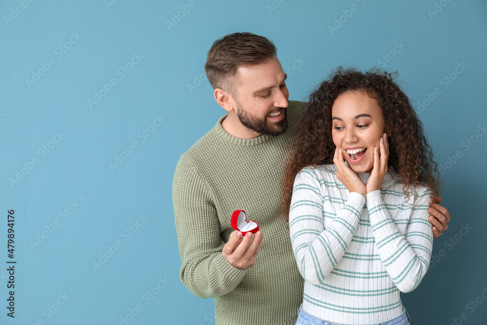 Young man proposing to his girlfriend on color background