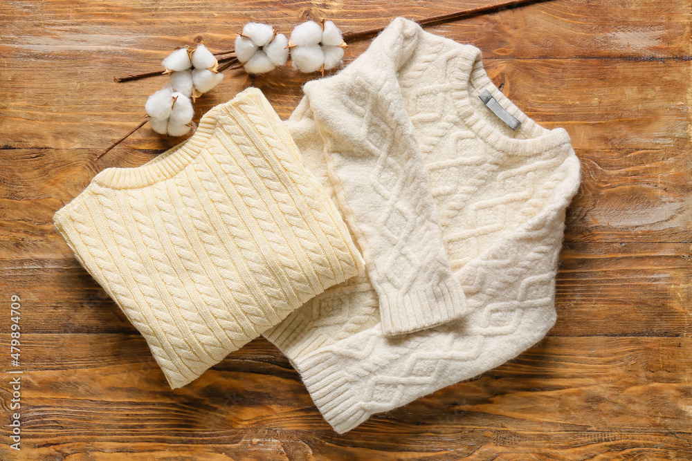 Childrens sweaters and branch of cotton flowers on wooden background