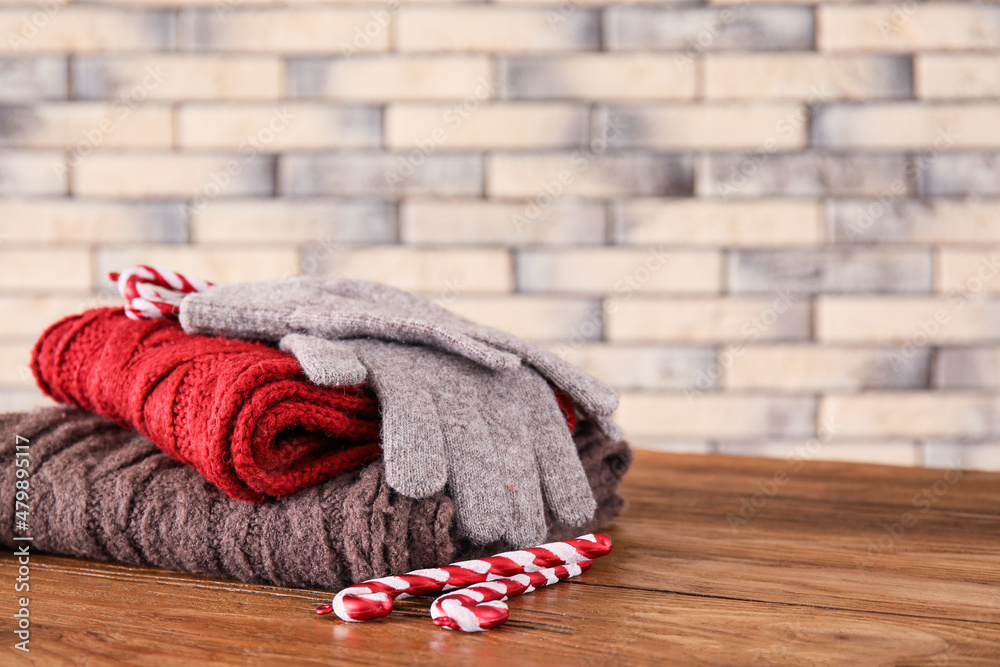 Knitted sweaters, gloves and candy canes on wooden table against brick wall background