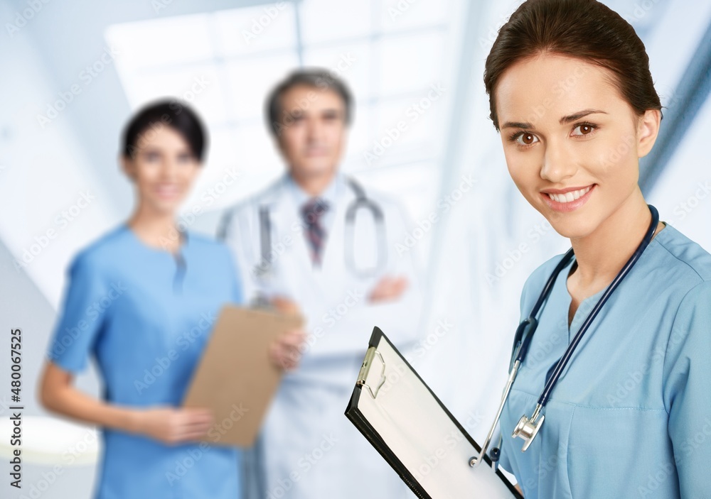 Portrait of happy young nurse in uniform with healthcare team in background. Successful doctor and n