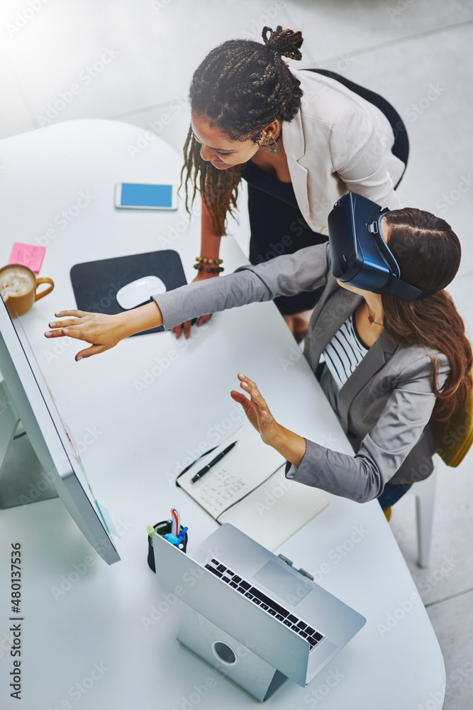 Tell me what you see. High angle shot of a young businesswoman using a VR headset while being assist