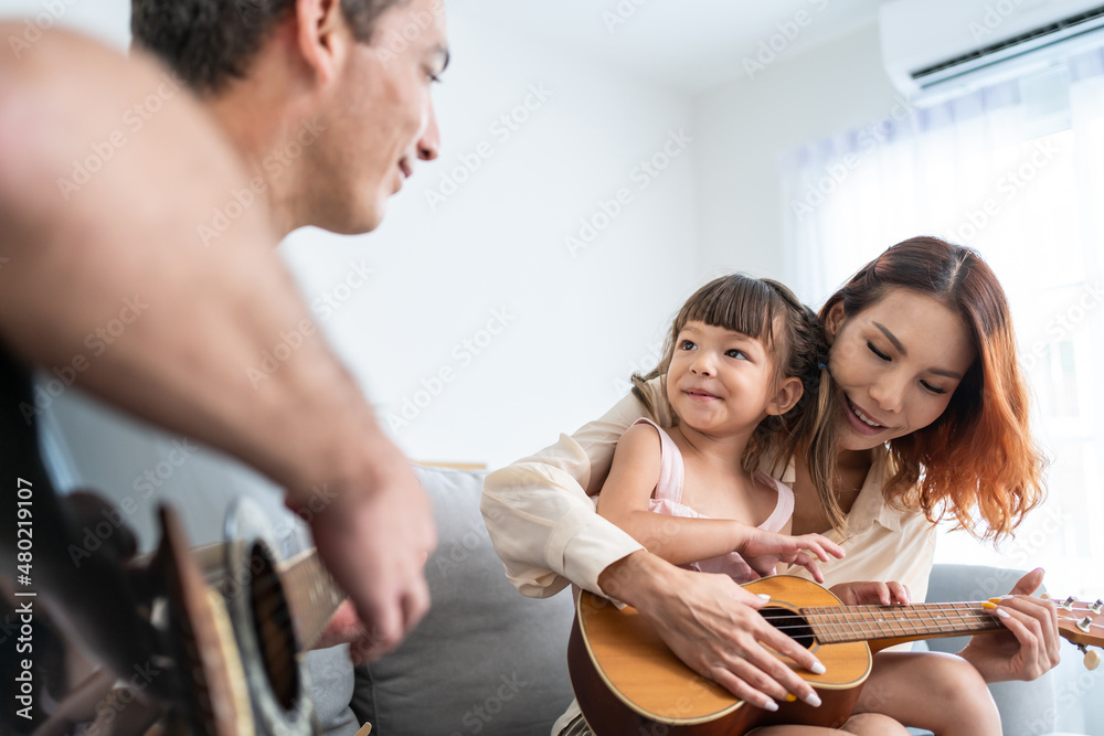 Asian young couple playing guitar with young baby kid together at home. 