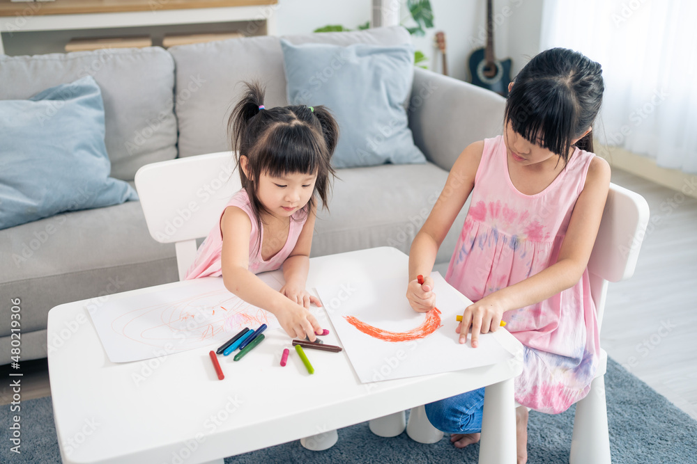 Asian young girl children drawing and coloring paper in living room. 