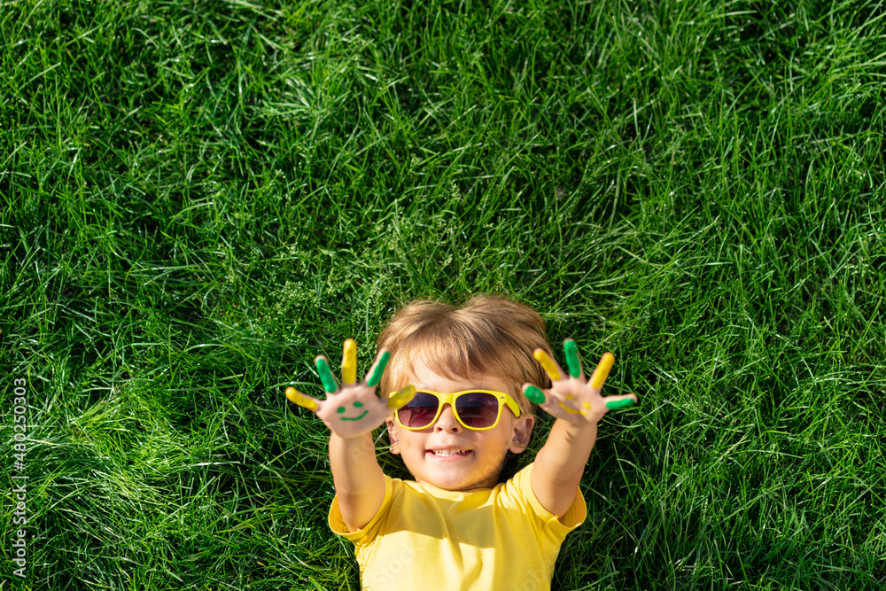 Happy child with smile on hands lying on green spring grass