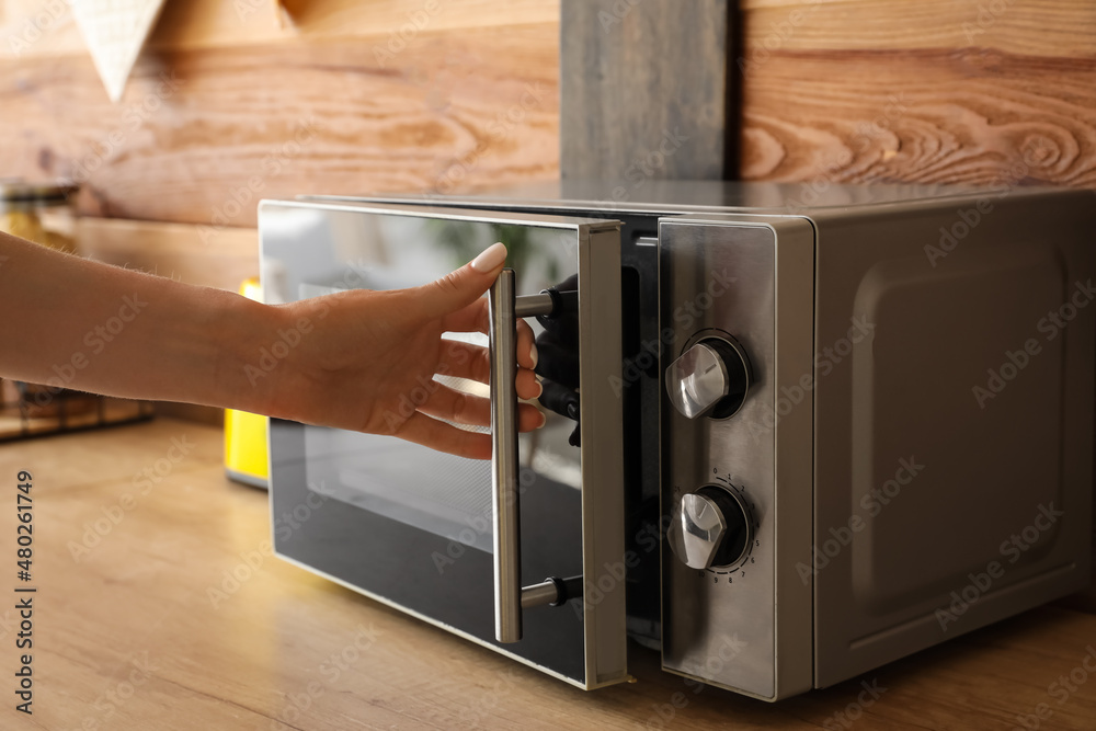 Woman opening microwave oven in kitchen, closeup