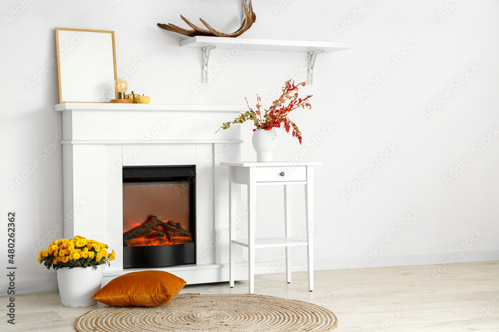 Interior of light room with modern fireplace, blank frame and vases