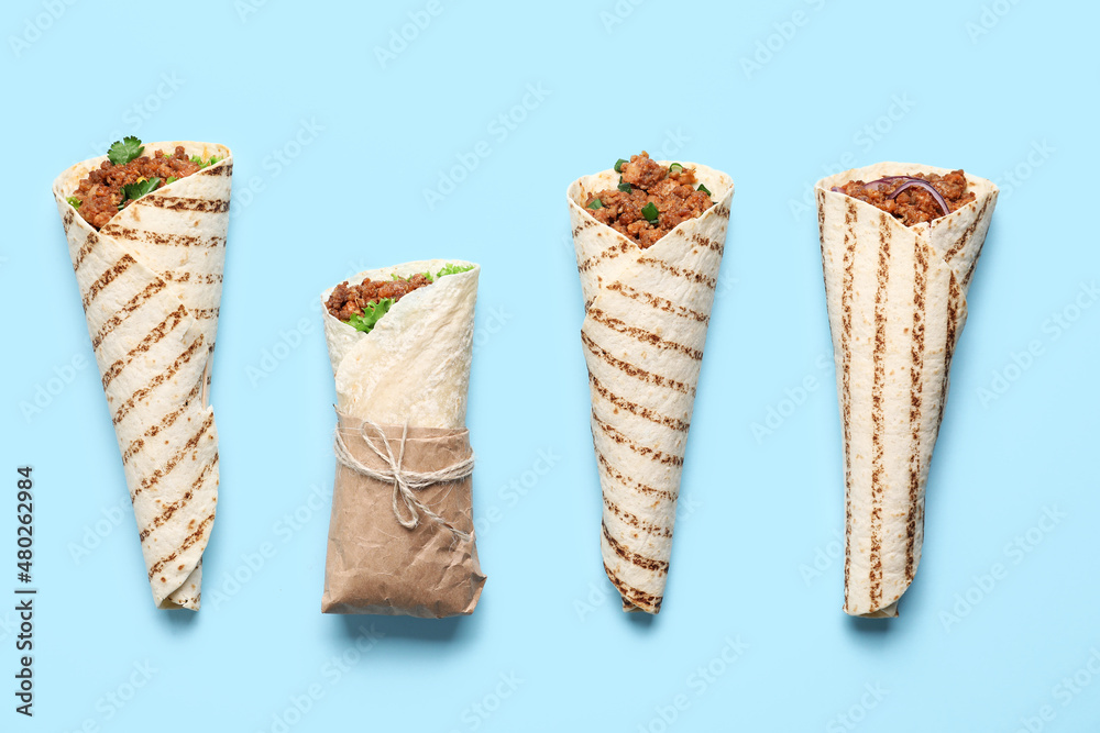 Different tasty burritos on blue background