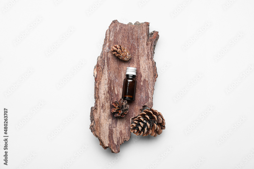 Bottle of essential oil, tree bark and cones on white background