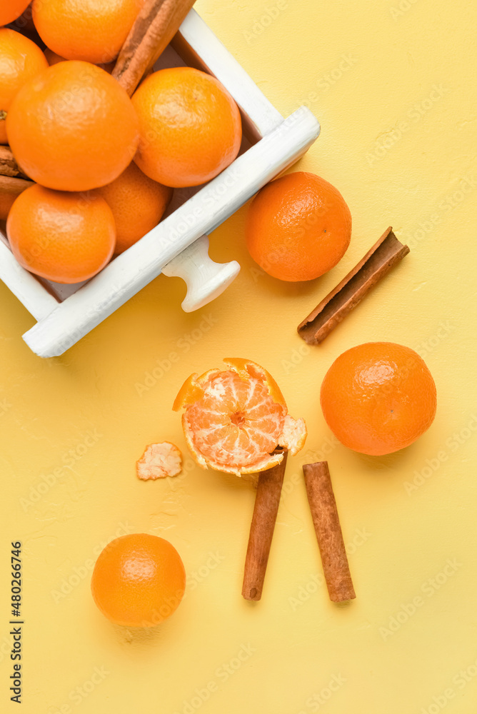 Wooden box with tasty tangerines on yellow background, closeup