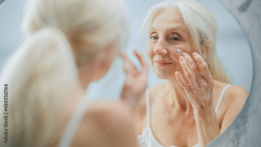 Portrait of Beautiful Senior Woman Morning Routine, Looking into Mirror Gently Applying Face Cream. 