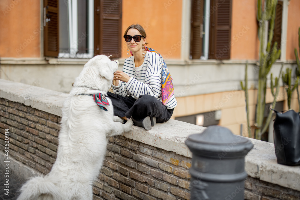 Young woman eating ice cream while sitting with her huge dog outdoors. Concept of italian street lif