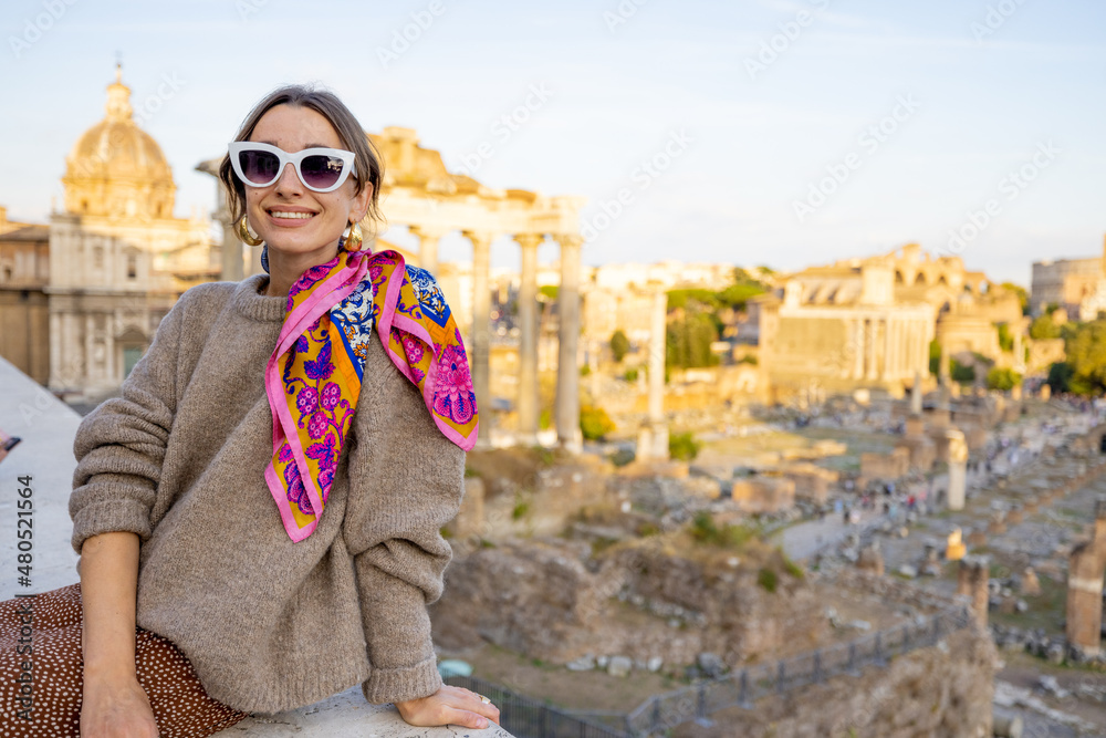 Portrait of a cheerful woman in front of the Roman Forum, ruins at the center of Rome on a sunset. C