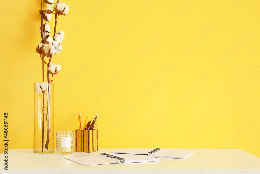 Stationery supplies, candle and cotton flowers on table near color wall