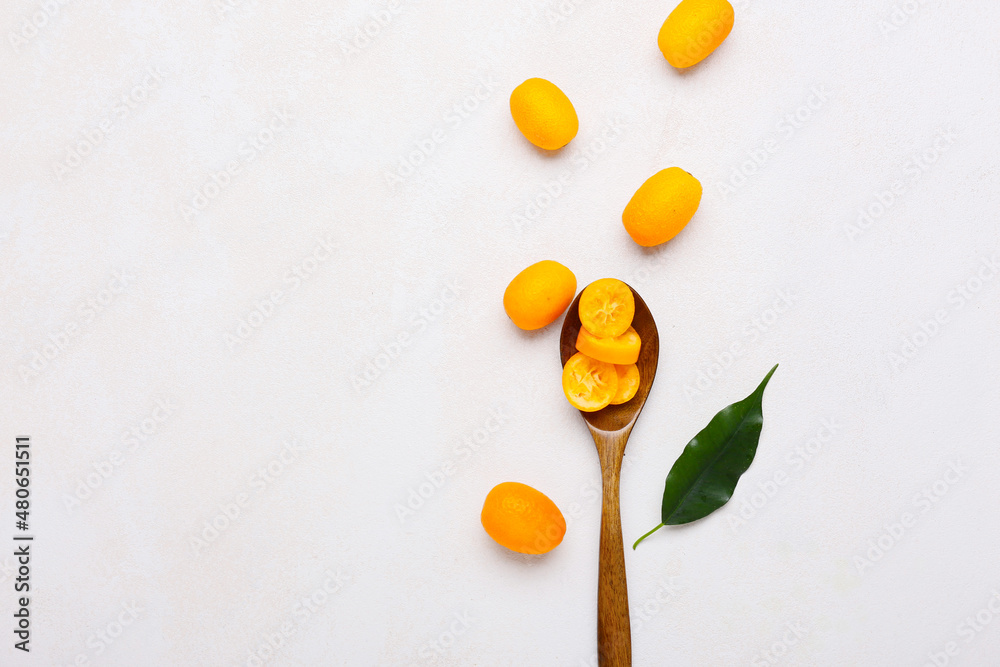 Spoon with tasty kumquat fruits on light background