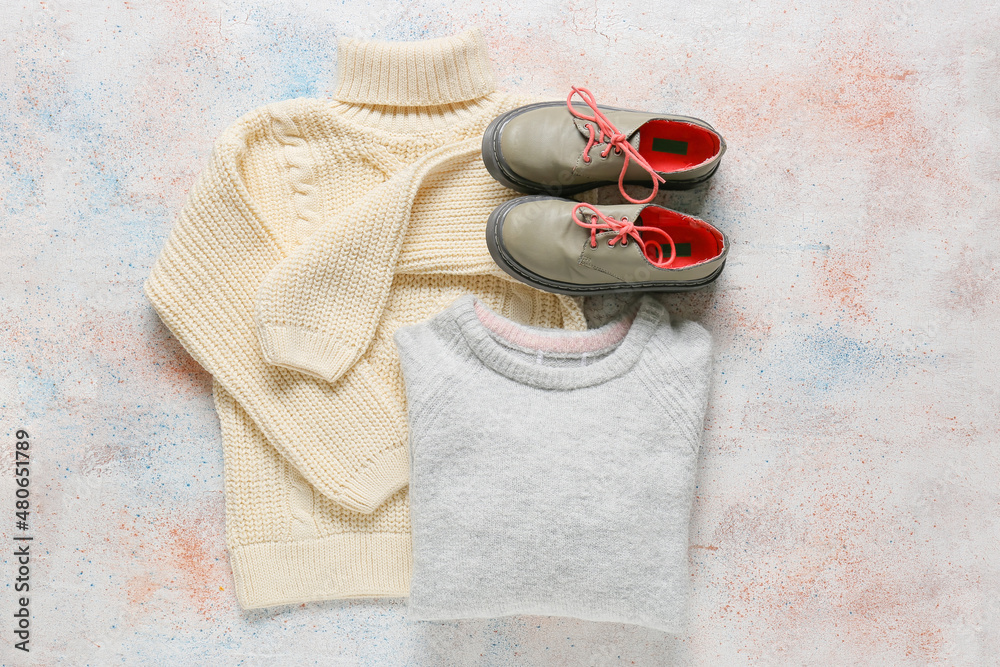 Warm childrens sweaters and shoes on light background