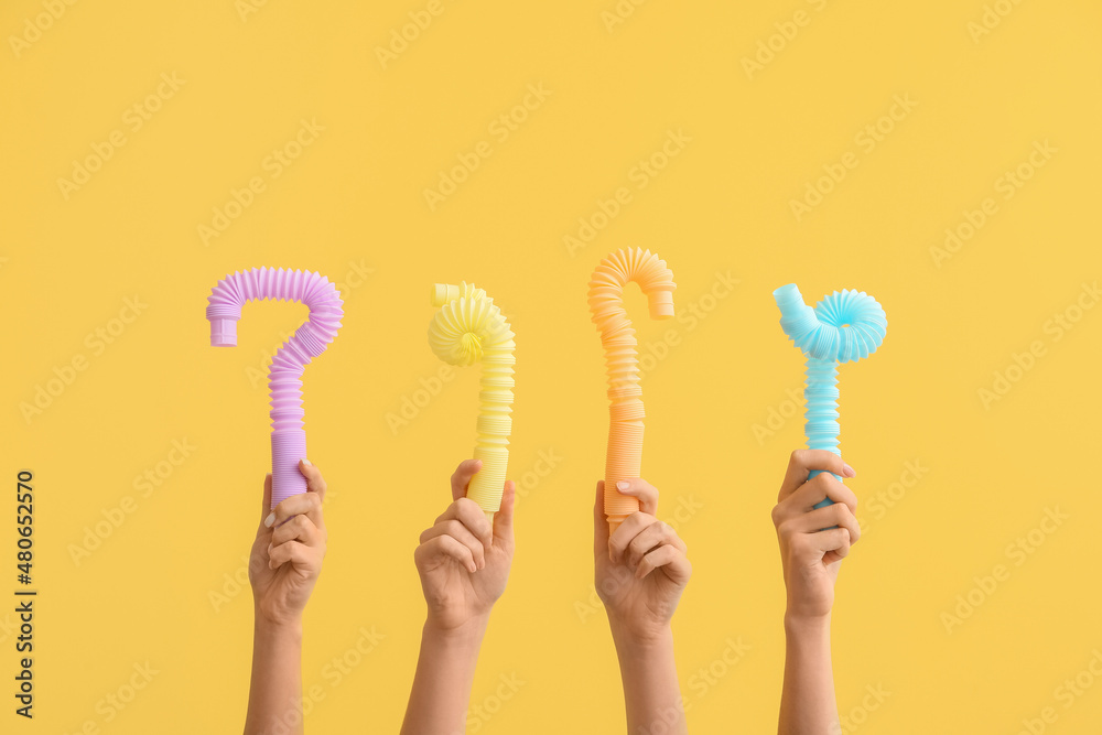 Hands with popular pop tubes on color background