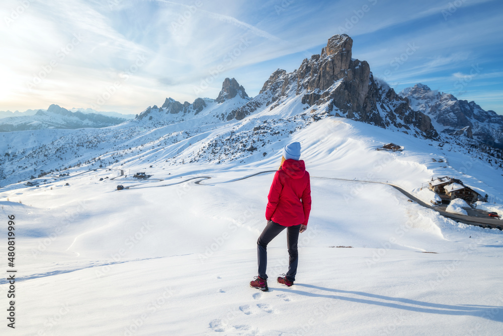 Young woman in red jacket in snowy mountains at sunset in winter. Landscape with beautiful girl on t