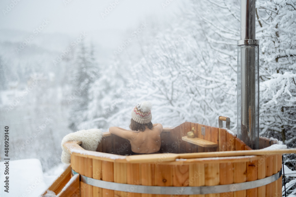 Woman relaxing in hot bath outdoors, sitting back and enjoying beautiful view on snowy mountains. Wi