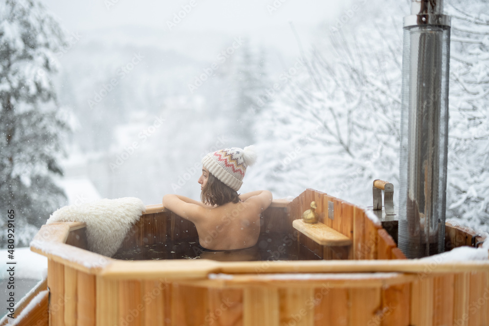 Woman relaxing in hot bath outdoors, sitting back and enjoying beautiful view on snowy mountains. Wi