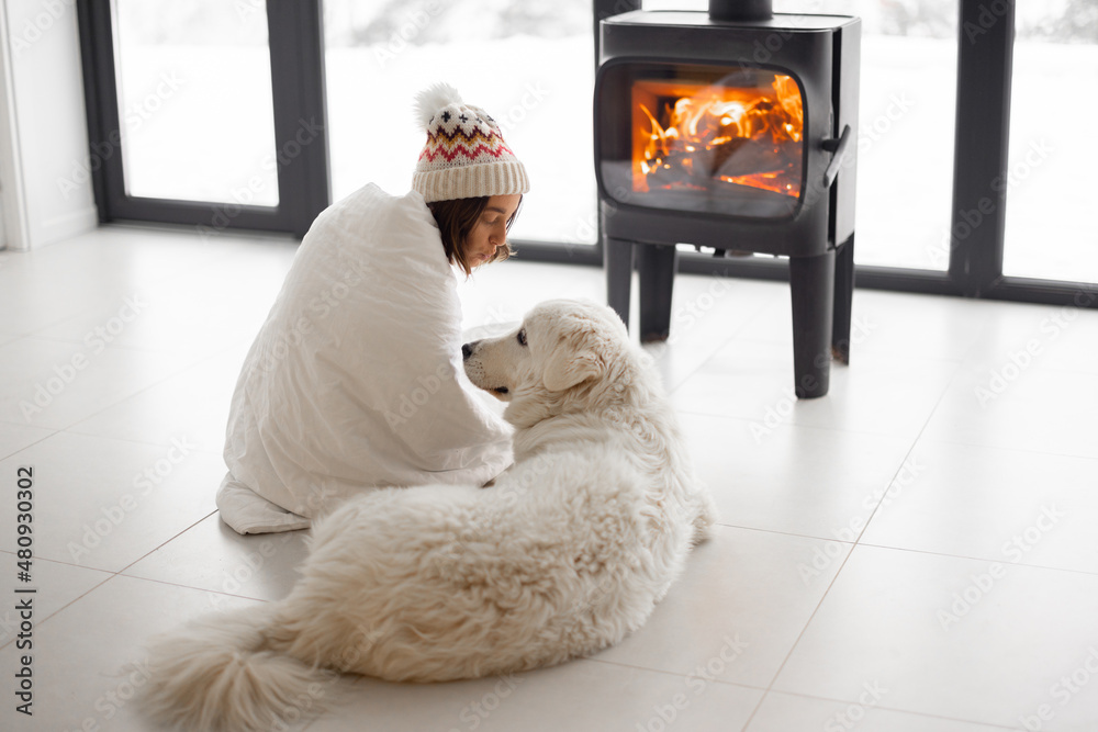 Woman sitting with her dog by the fireplace at modern house on nature during winter time. Concept of