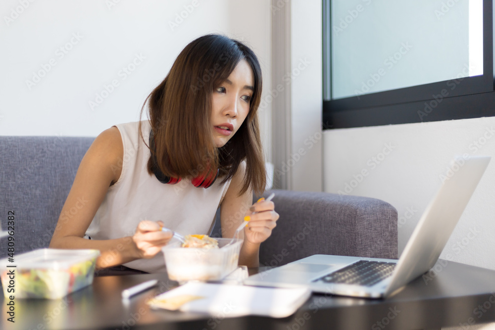 女性白天在家用笔记本电脑工作时吃午饭。在家工作和保持社交距离