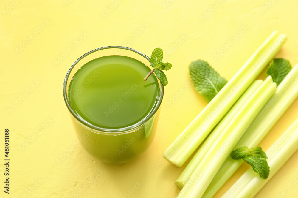 Glass of healthy green juice and fresh celery on yellow background