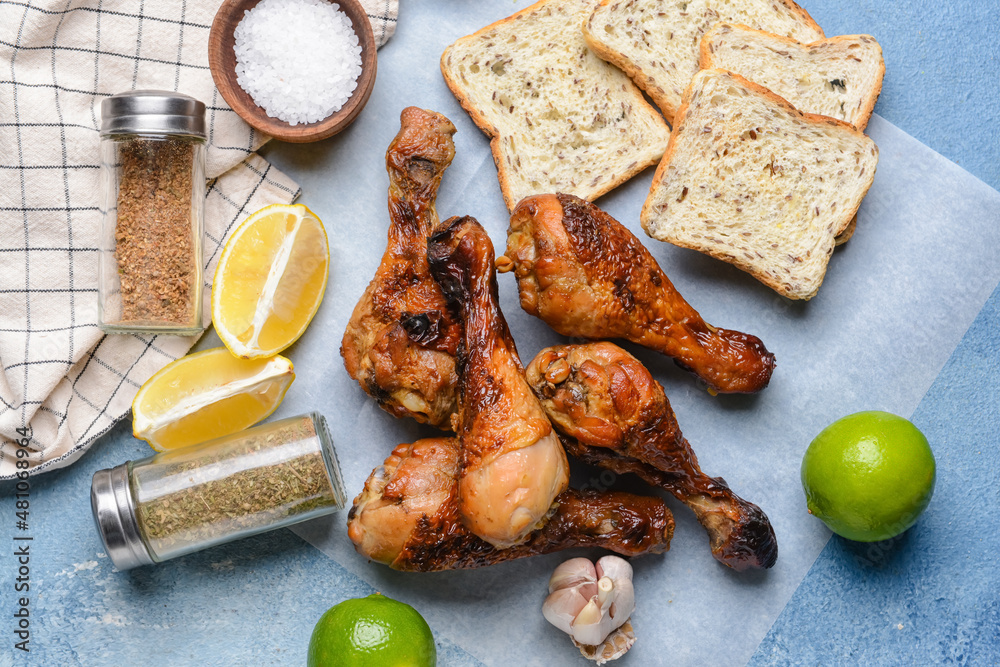 Tasty cooked chicken drumsticks with bread and spices on color background